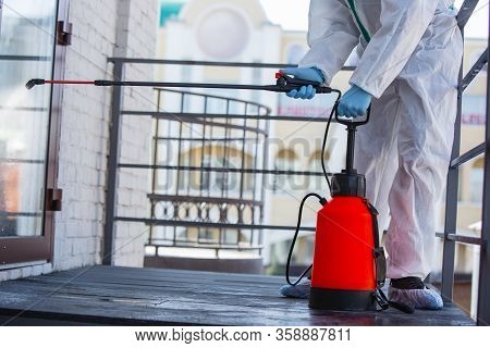 Coronavirus Pandemic. A Disinfector In A Protective Suit And Mask Sprays Disinfectants In House Or O