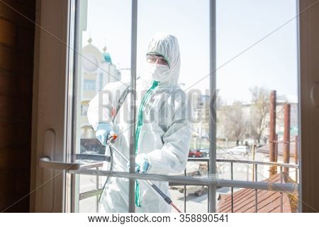 Coronavirus Pandemic. A Disinfector In A Protective Suit And Mask Sprays Disinfectants In House Or O