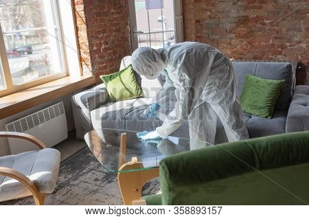 Coronavirus Pandemic. A Disinfector In A Protective Suit And Mask Sprays Disinfectants In House Or O