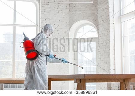 Coronavirus Pandemic. A Disinfector In A Protective Suit And Mask Sprays Disinfectants In House Or O