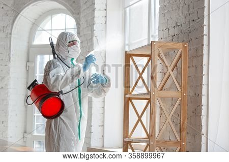 Coronavirus Pandemic. A Disinfector In A Protective Suit And Mask Sprays Disinfectants In House Or O