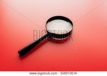 Close Up Single Magnifying Glass With Black Handle, Leaning On The Red Table At The Office.