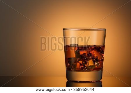 A Glass Of Whiskey With Ice On A Dark Surface With A Reflection. Space For Text