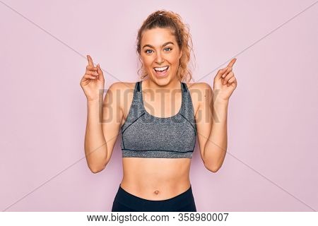 Young beautiful blonde sportswoman with blue eyes doing exercise wearing sportswear smiling amazed and surprised and pointing up with fingers and raised arms.