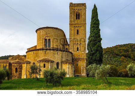Picturesque Tuscany. Tall slender cypress adorns the meadow around the abbey. Ancient medieval magnificent abbey of San Antimo. The concept of active, rural and photo tourism