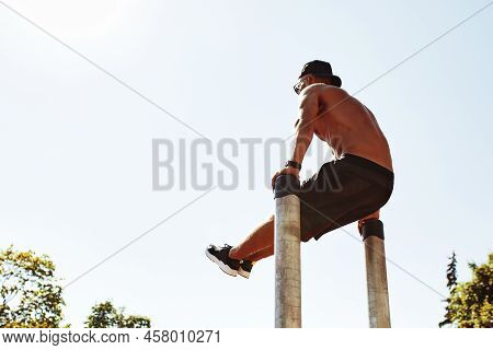 Athletic Sportsman Trains On The Horizontal Bars. Training At The Open Air Sprorts Ground.