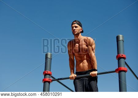 Athletic Sportsman Trains On The Horizontal Bars. Training At The Open Air Sprorts Ground.