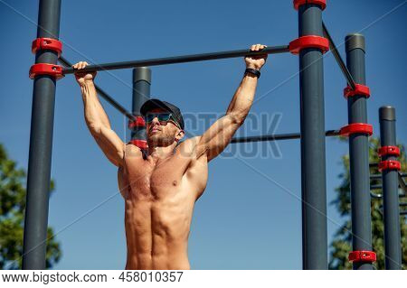 Athletic Sportsman Trains On The Horizontal Bars. Training At The Open Air Sprorts Ground.