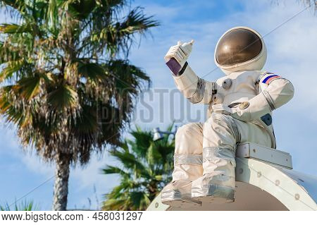 A Cute Figurine Of An Astronaut In A Spacesuit Holding A Tube Of Food In His Hand Sits Against The B