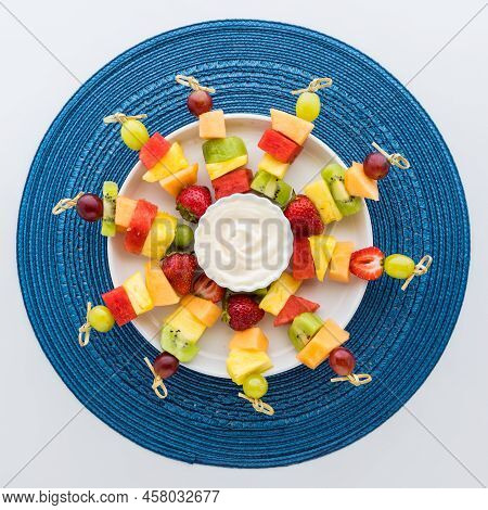 A Round Platter With Fresh Fruit Skewers And Yogurt Dip In The Middle.
