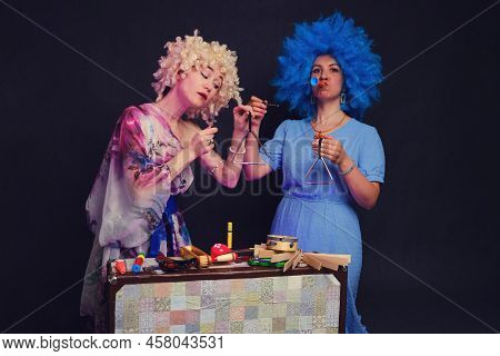 Happy Women In Funny Wigs Give A Musical Performance On A Studio Black Background. Smiling Women Sho