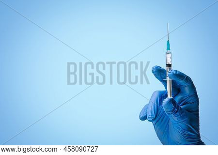 Doctors Hand In Surgical Gloves Holds A Syringe On A Classic Symbolic Blue Background