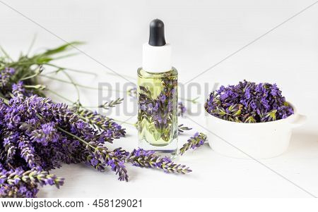 Glass Bottle Of Lavender Essential Oil With Fresh Lavender Flowers And Dried Lavender Seeds On White