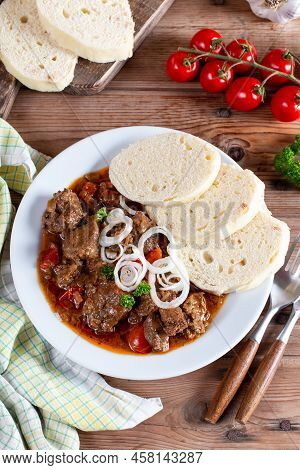 Pork Goulash Meat With Dumplings On White Plate, Cutlery, Garlic, Onion, Pepper, Tablecloth In The B