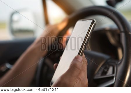 The Driver\'s Hand Behind The Wheel Holds A Smartphone. Navigator, Satellite Navigation, Communicati