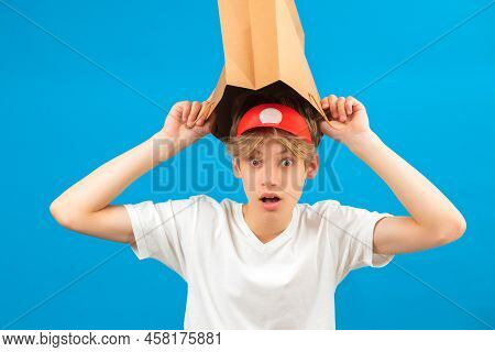 Shocked Teen Boy With Paper Bag Over Head. Teenager Holding Paper Bag Over The Head Posing In Studio
