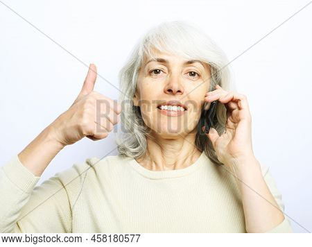 Modern Lifestyle, Tehnology And Old People Concept: Photo Of Old Woman Use Smartphone And Show Thumb