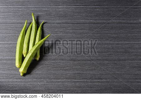 Fresh Ochra, Bhindi Or Ladies Fingers Whole And Uncooked Against A Grey Horizontal Stripped Backgrou