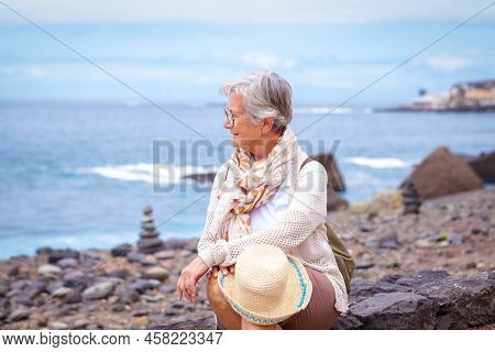 Portrait Of Relaxed Caucasian Woman With Hat Sitting At The Beach Looking Away While Enjoying Vacati
