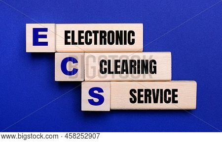 On A Bright Blue Background, Light Wooden Blocks And Cubes With The Text Ecs Electronic Clearing Ser