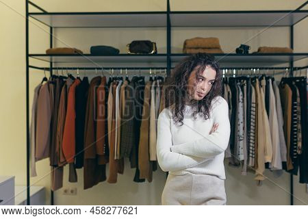 Upset And Sad Young Woman Standing In A Clothing Store In A Shopping Center, Hands Folded, Dissatisf