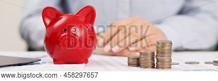 Close-up Of Person Accountant On Working Place, Stack Of Coins, Red Piggy Bank. Prepare Annual Repor