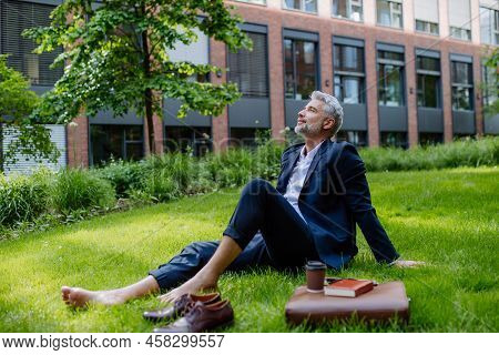 Mature Businessman Resting And Sitting Barefoot In Park, Feeling Free, Escaping From Work, Work Life