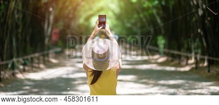 Asian Woman In Yellow Dress And Hat Traveling At Green Bamboo Tunnel, Happy Traveler Taking Photo By
