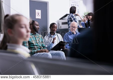 Selective Focus On African American Doctor With Stethoscope Completing Form For Patients In Waiting 