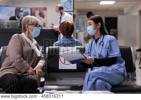 Diverse People Talking In Waiting Room Lobby, Doong Checkup Consultation During Coronavirus Epidemic