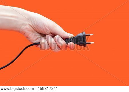 Electric Plug For A Socket In A Hand On An Orange Background. The Concept Of Electricity And Its Imp
