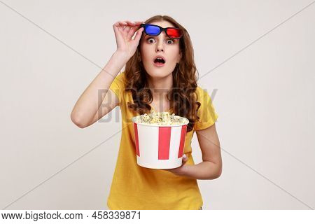 Image Of Beautiful Shocked Young Woman With Curly Hair In Yellow T-shirt Holding Popcorn Bucket, Rai