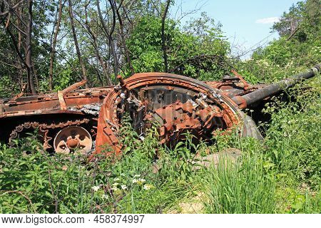 A Charred Tank With A Torn-off Turret In The Green Grass. A Blown Up And Burnt Tank At The Front. Wa