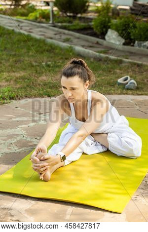 Young Woman Practices Yoga In The Garden. Yoga Pose Half Bound Lotus Seated Forward Extension. Ardha