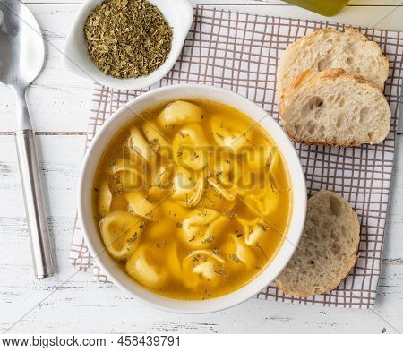 Cappelletti Or Tortellini Brodo Soup In A Bowl With Bread Slices And Seasoning Over Wooden Table.