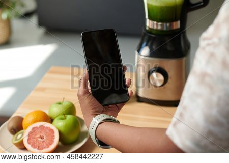Close-up Of Girl Using Her Smartphone To Turn On The Blender Online And Do Fresh Smoothie