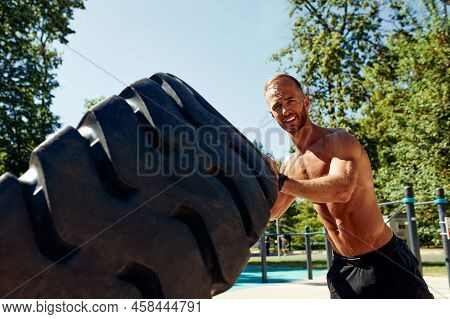 Strong Man Training Workout Lifting Large Tire Outdoor Gym. Sportive Young Adult Caucasian Guy Flip 