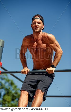 Athletic Sportsman Trains On The Horizontal Bars. Training At The Open Air Sprorts Ground.
