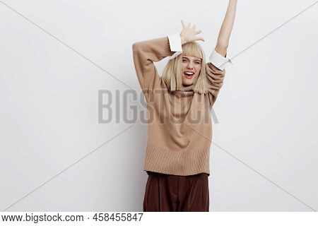 An Attractive Happy Woman Stands On A Light Background In A Sweater And Shirt, Enthusiastically Jump