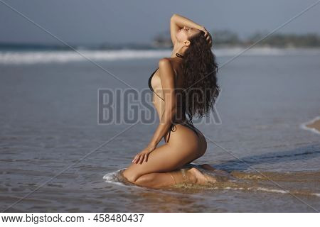Fashion Shot Of A Gorgeous Young Adult Woman Model In A Trendy Black Bikini Sitting In An Erotic Pos