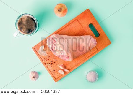 Raw Pork Knuckle, Garlic, Onion, Dried Bay Leaves, Sea Salt And Peppercorns On Wooden Cutting Board.
