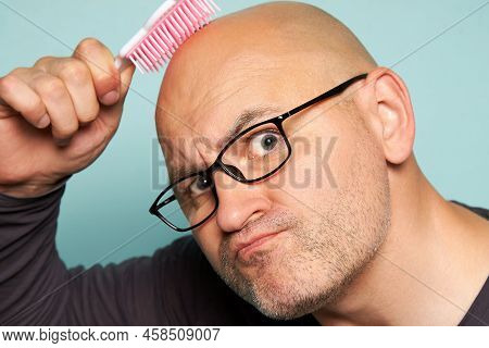 Bald Bearded Man With Glasses Is Fooling Around In Front Of The Camera With A Baby Comb On A Turquoi