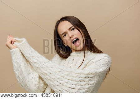 A Cheerful Woman Standing Sideways On A Light Brown Background In A White Sweater Raised Her Hands A