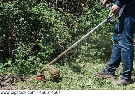 The Man Mowing Green Wild Grass Using Brush Cutter Mower Or Power Tool String Lawn Trimmer. To Mow A