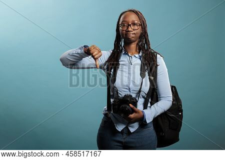 Disapproving Photographer Giving Thumbs Down Gesture At Camera While Standing On Blue Background. Yo