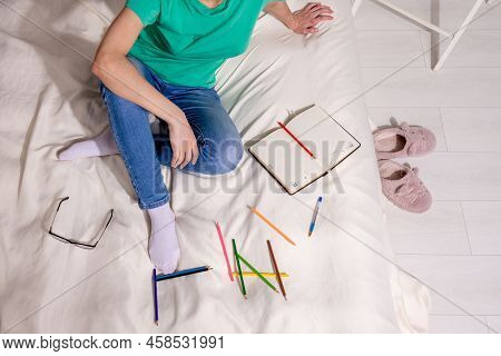 A Girl In A Green T-shirt And Blue Jeans Is Sitting On The Bed And Writing In A Notebook, Colored Pe