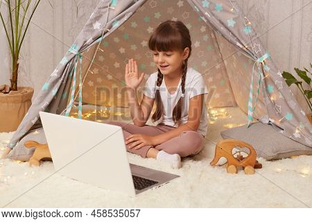 Image Of Cute Little Girl Sitting In Wigwam On Floor On Soft Carpet Having Video Call On Laptop Rais
