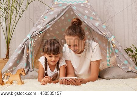 Horizontal Shot Of Woman And Her Daughter Laying In Peetee Tent And Watching Cartoons On Mobile Phon