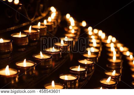 Close-up Shot Of Prayer Candles The Darkness In A Church. Small Wax Lighted Candles As Symbol Of Fai