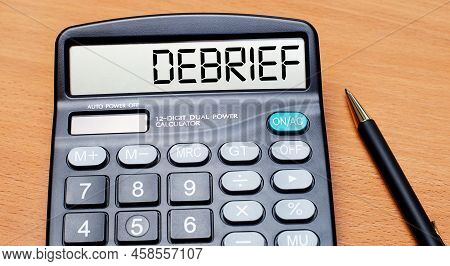 On A Wooden Table There Is A Black Pen And A Calculator With The Text Debrief. Business Concept